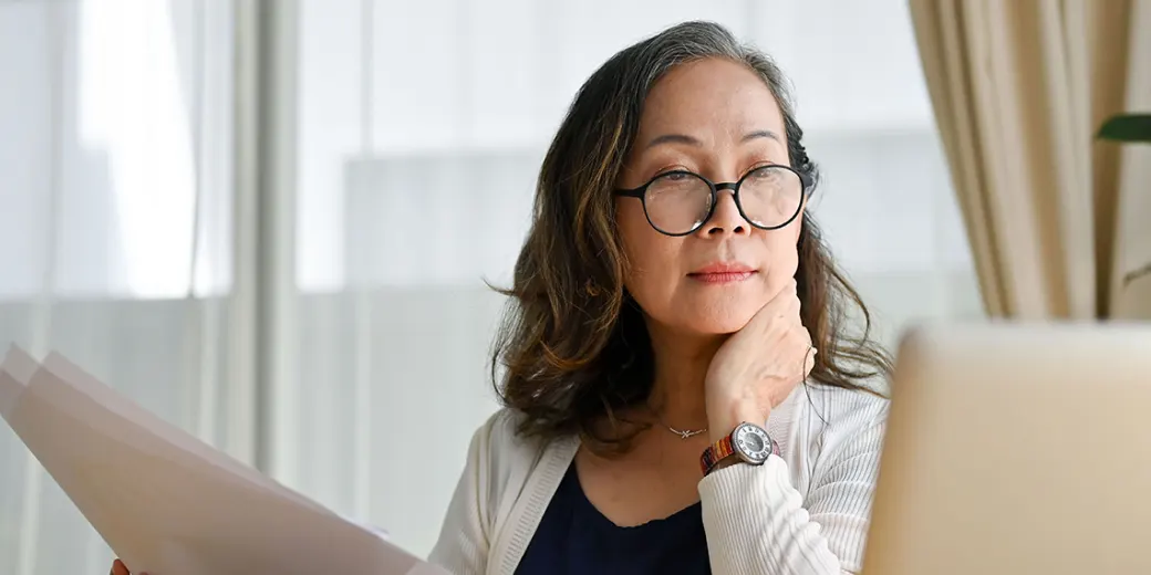 Older woman with papers in hand looking at computer