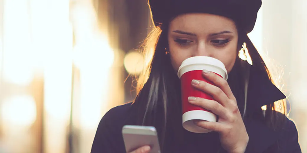 Woman with red coffee cup looking at phone